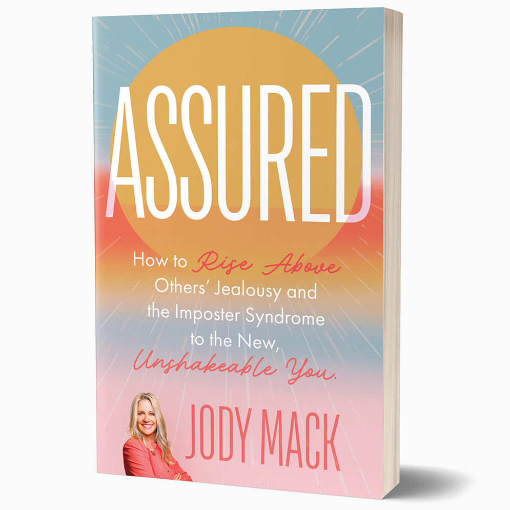 The paperback edition of Assured, standing at a 3/4 angle with page edge showing.